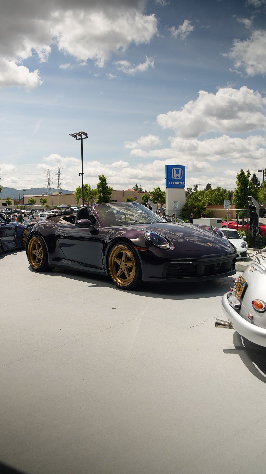 A glossy purple Porsche with gold wheels parked at a car show, with a Honda sign in the background.