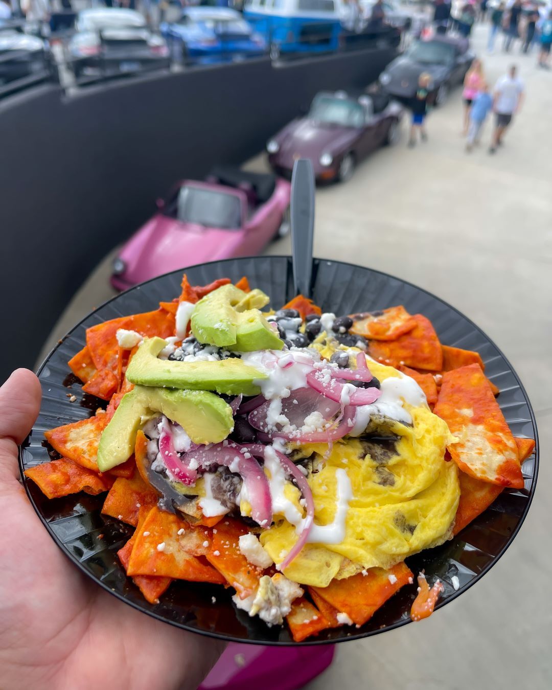 Chilaquiles with scrambled eggs, avocado, black beans, red onion, crema, and cheese in a black bowl.