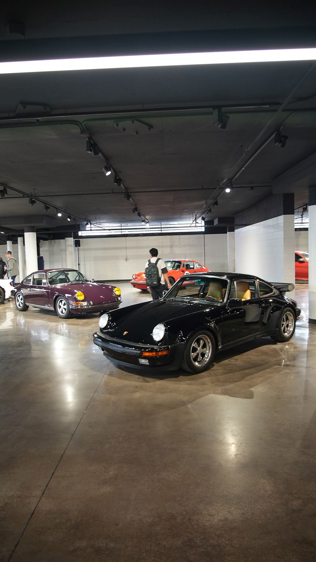 A black vintage Porsche 911 in the foreground, with a purple Porsche 911 behind it in a showroom.