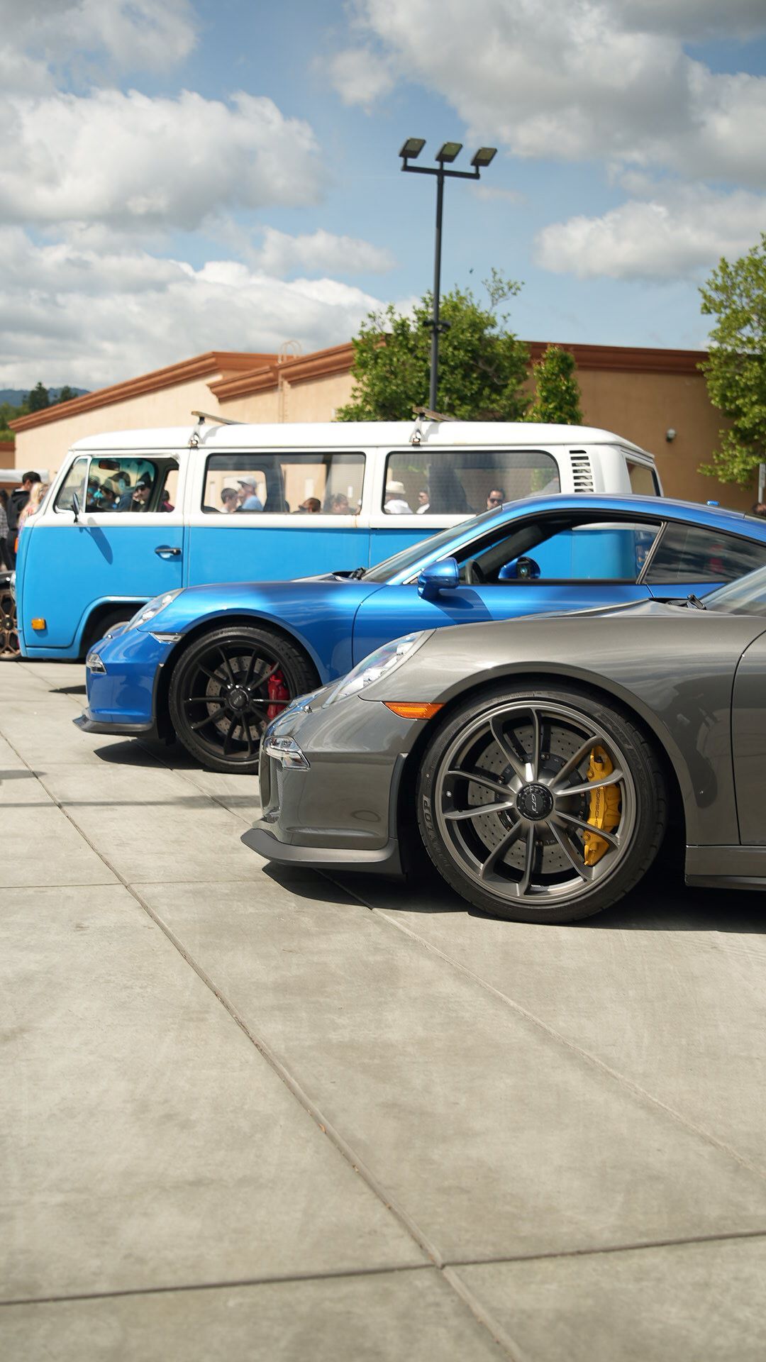 A grey sports car and blue identical car parked behind it, with an old blue and white camper van behind them.