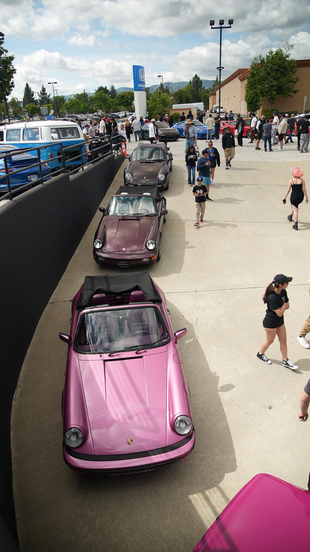 Overhead view of a car show with a bright pink convertible in the foreground and a line of maroon cars.