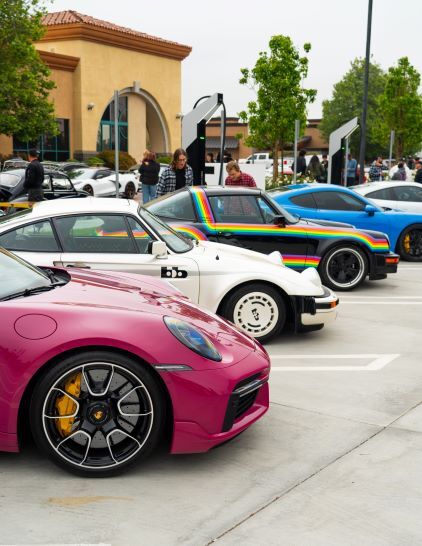 Colorful vintage Porsche cars are displayed in a row at an outdoor car show.
