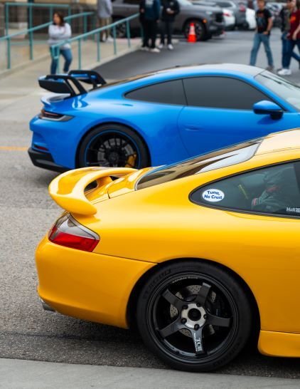 A bright blue sports car and yellow modified car are parked at a car show.
