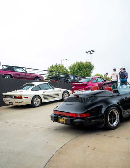 Several classic Porsche cars are parked at an outdoor car show, with people viewing them.