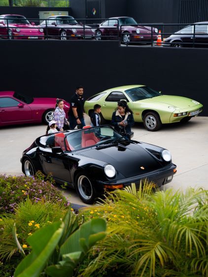 Several people admire a display of classic Porsche cars parked in front of a dark building.