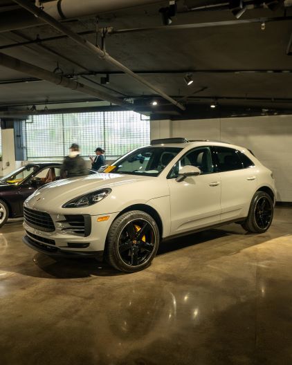 A white Porsche Macan SUV sits in a dimly lit parking garage, with people standing nearby.