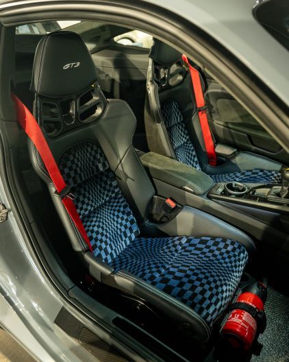 A gray Porsche GT3 interior features racing seats with red harness belts and a blue checkered pattern.