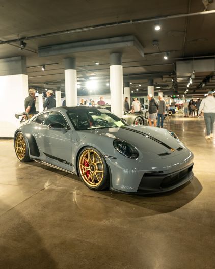 A sleek gray Porsche 911 GT3 with gold wheels and red brake calipers is displayed indoors on a polished floor.