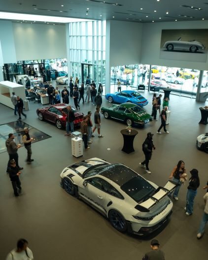 People browse luxury cars displayed in a modern, spacious showroom with large windows.