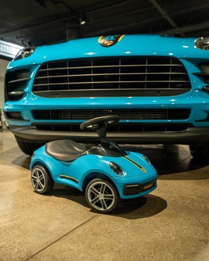 A bright blue Porsche car sits in front of a miniature, matching toy car.