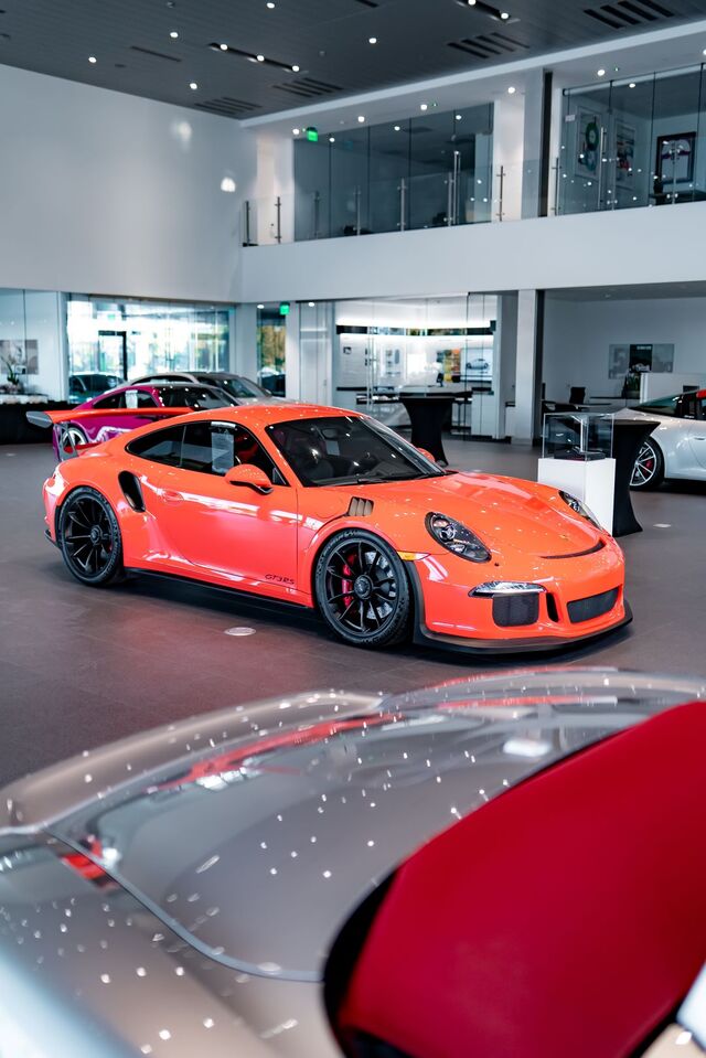 Orange Porsche GT3 RS with black wheels on display in a modern, brightly lit car showroom.