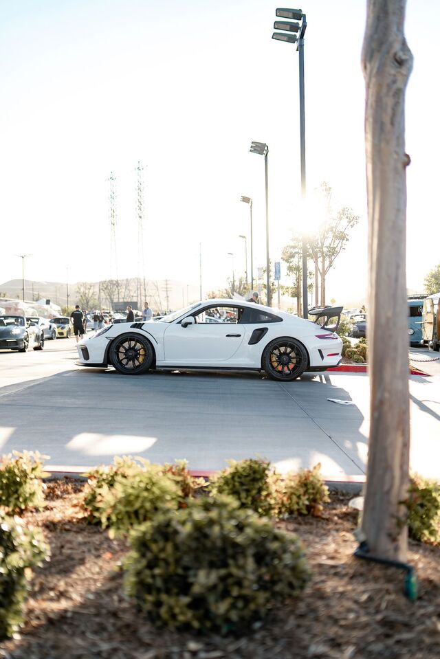 Side view of a white Porsche 911 GT3 RS parked with other cars at an outdoor event on a sunny day.