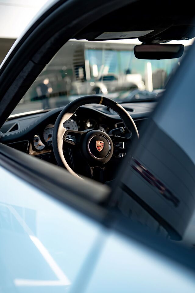 View into a modern Porsche's interior, showing its black and tan steering wheel with the Porsche emblem.