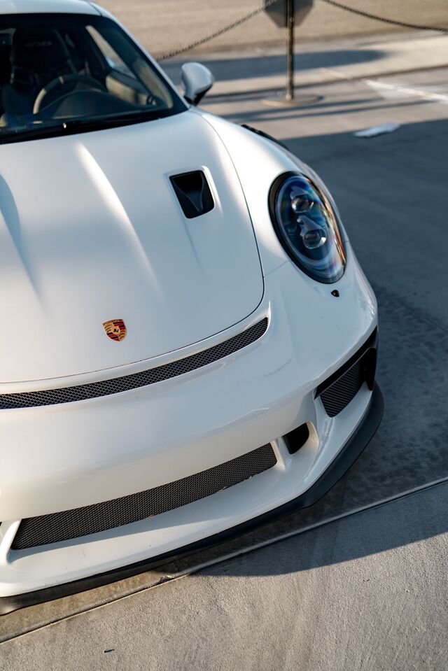 Close-up of the front of a white Porsche 911 GT3 parked on concrete.