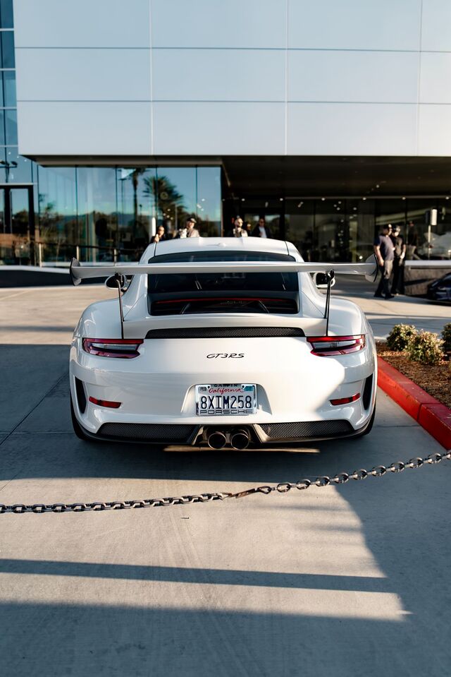 A white Porsche GT3 RS sits parked in a lot with a large spoiler and California license plate.