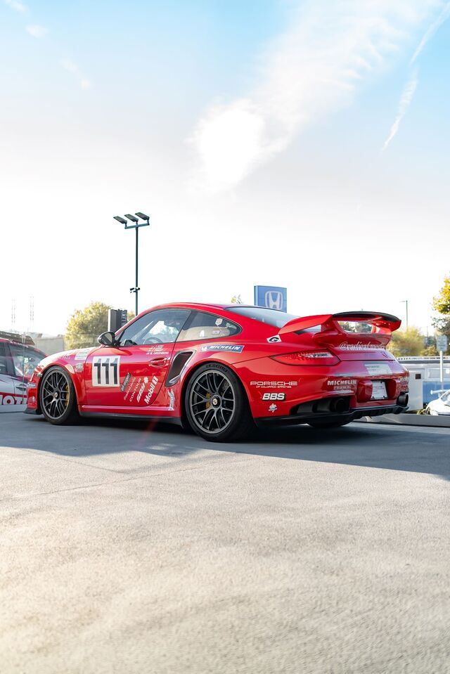 Side view of a red Porsche 911 GT3 RS race car with '111' on the door, parked on asphalt.