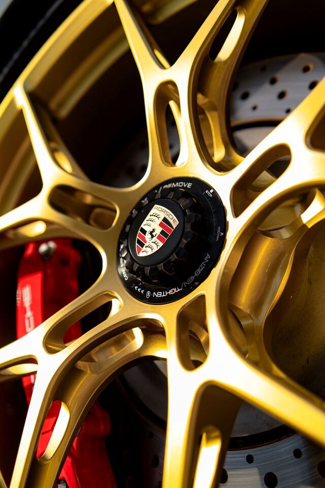 Close-up of a gold Porsche wheel with the Porsche crest on the center cap, red brake caliper visible.