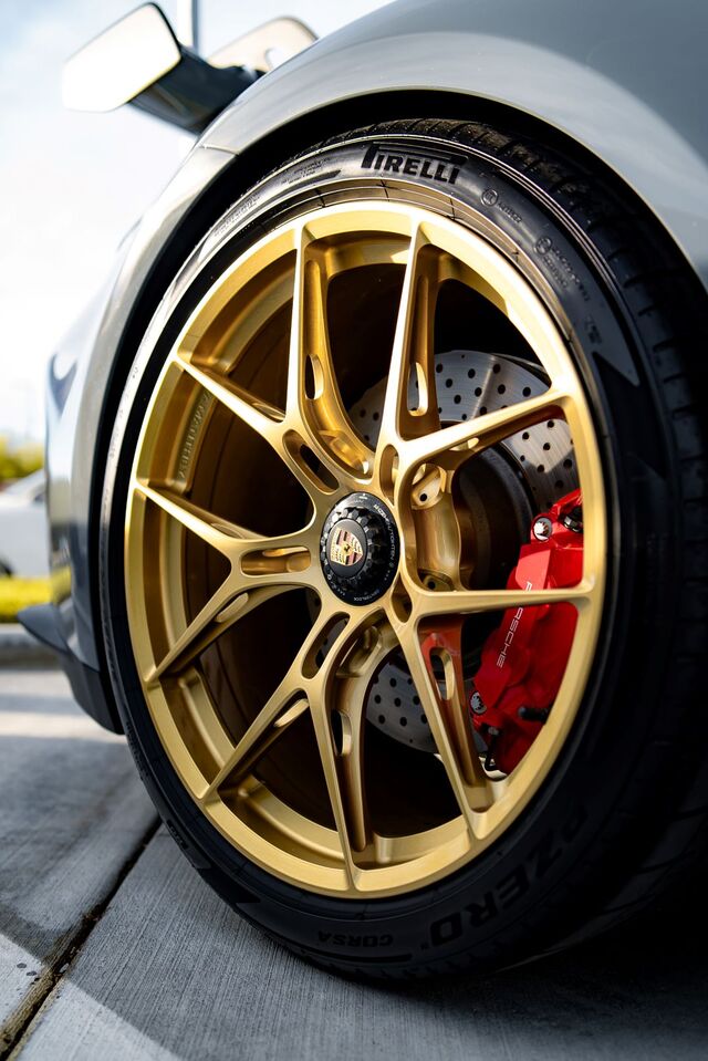 Close-up of a Porsche car's tire with gold multi-spoke rim, red brake caliper, and a silver disc brake.