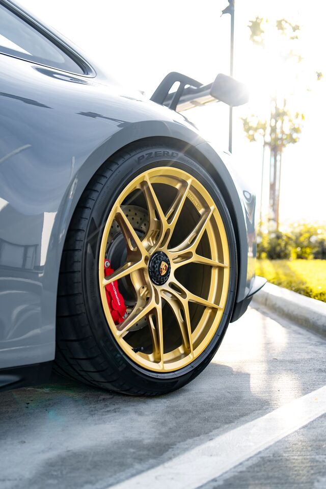 A gray Porsche sports car sits parked, showcasing its gold-colored wheels and red brake calipers.