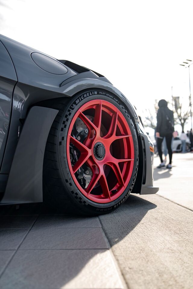 Close-up of a sleek gray sports car's front fender and bright red multi-spoke wheel with Michelin tire.