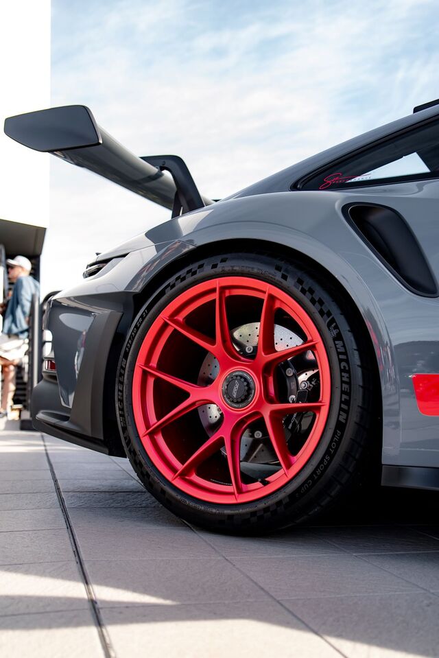 A gray sports car with red rims and a prominent wing sits parked on pavement.