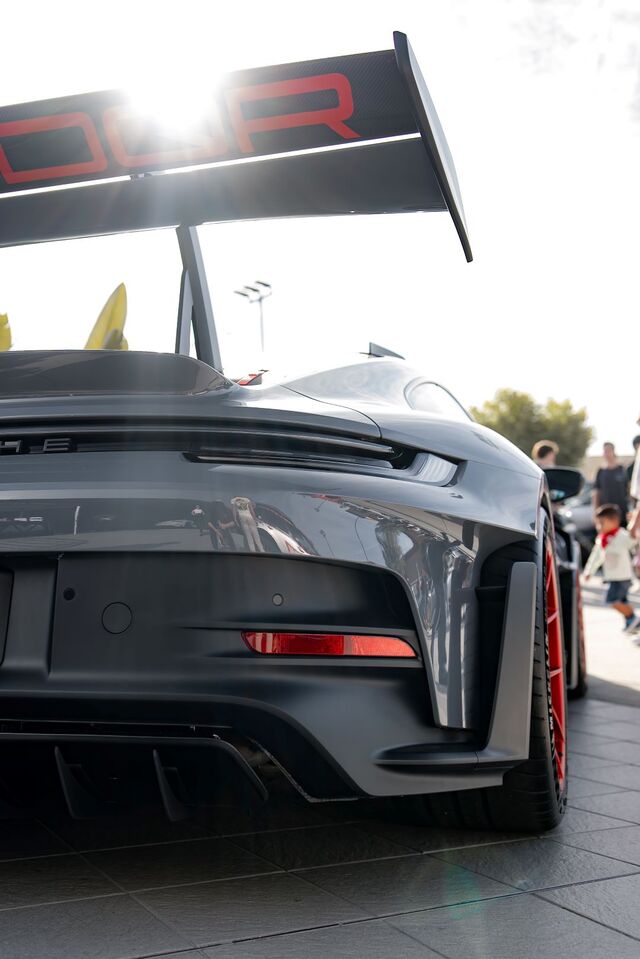 Rear view of a grey Porsche GT3 RS with a large spoiler, red wheels, and lens flares from the sun.