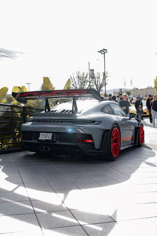 Rear view of a grey Porsche GT3 parked on a tiled surface, with red wheels and a large spoiler.