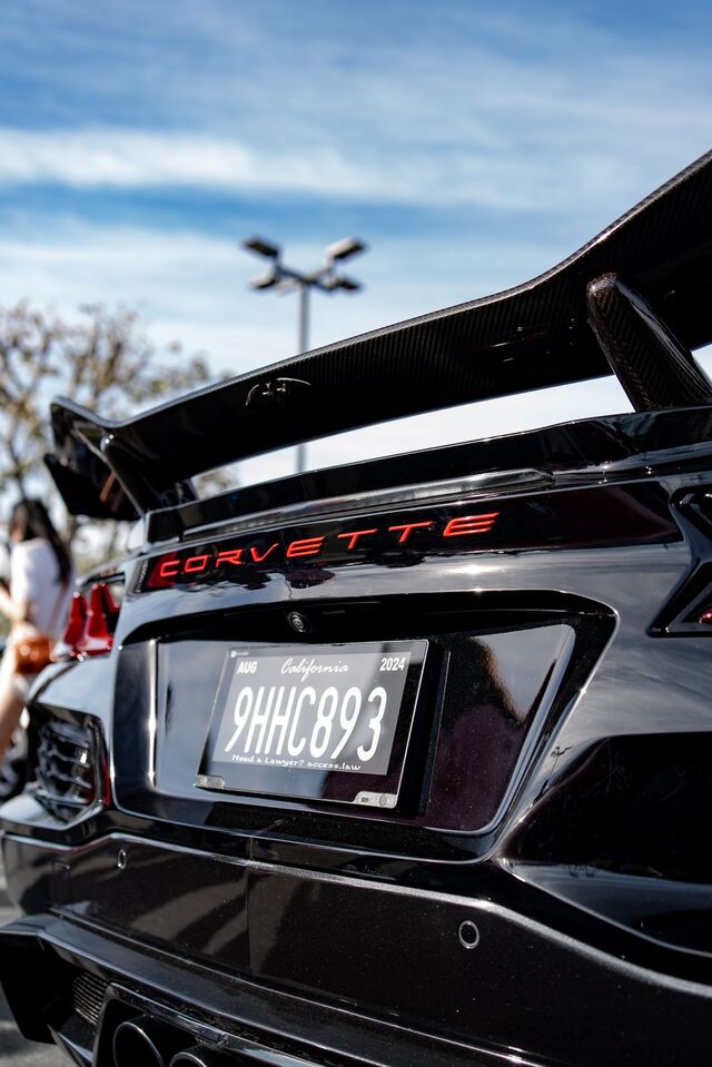 Rear view of a black Corvette with a large carbon fiber spoiler, red 'Corvette' emblem, and California license plate.