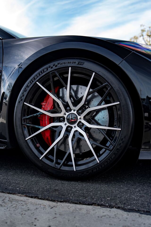 A black car's wheel showcases a white and gray spoke design with red brake calipers and Michelin tires.