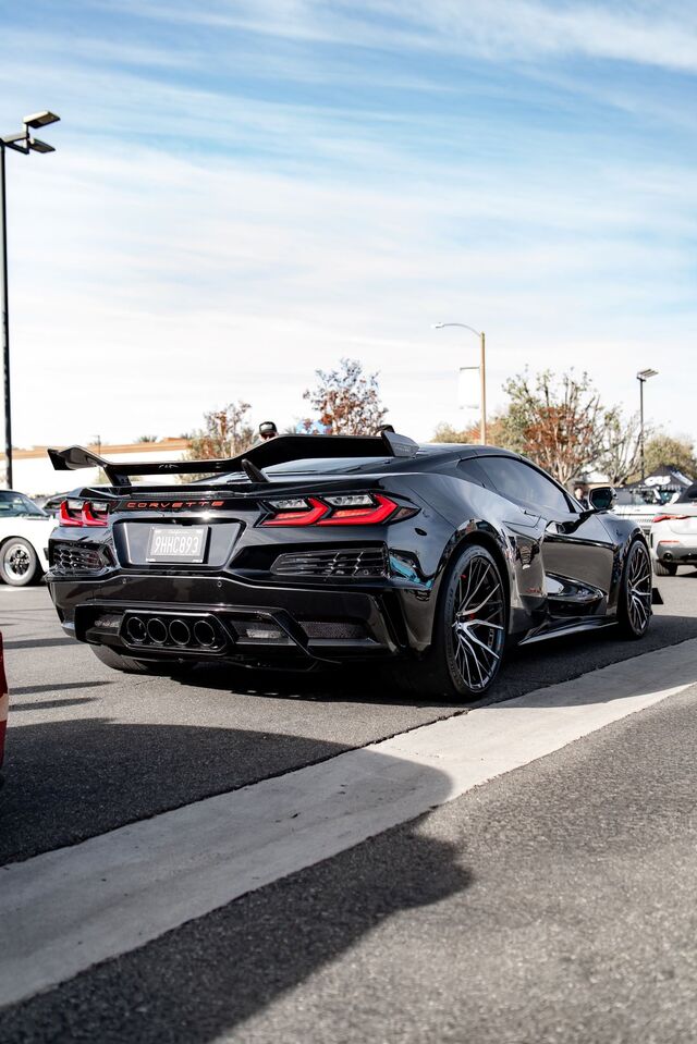 A black Chevrolet Corvette with a large spoiler is parked in a lot with other cars.