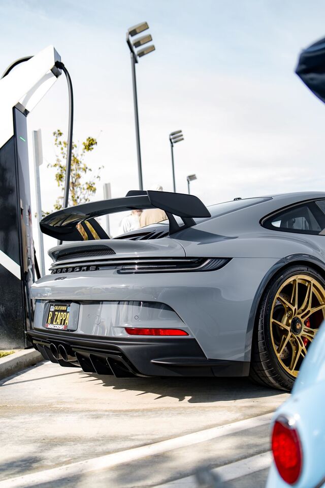 A silver Porsche 911 GT3 is parked at an electric vehicle charging station.
