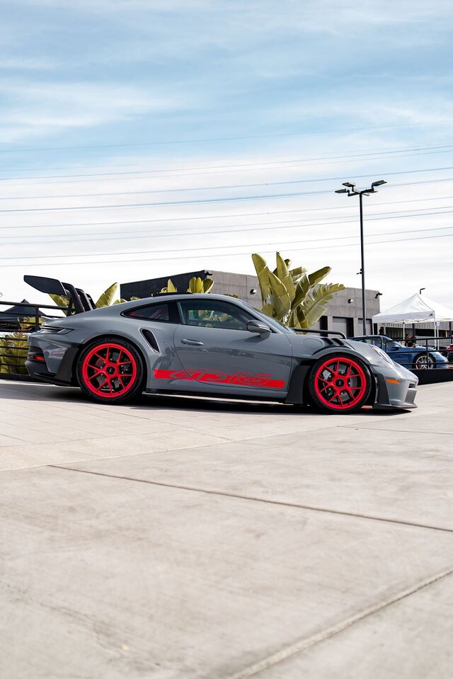 A gray Porsche 911 with bright red wheels and spoiler sits parked on pavement.