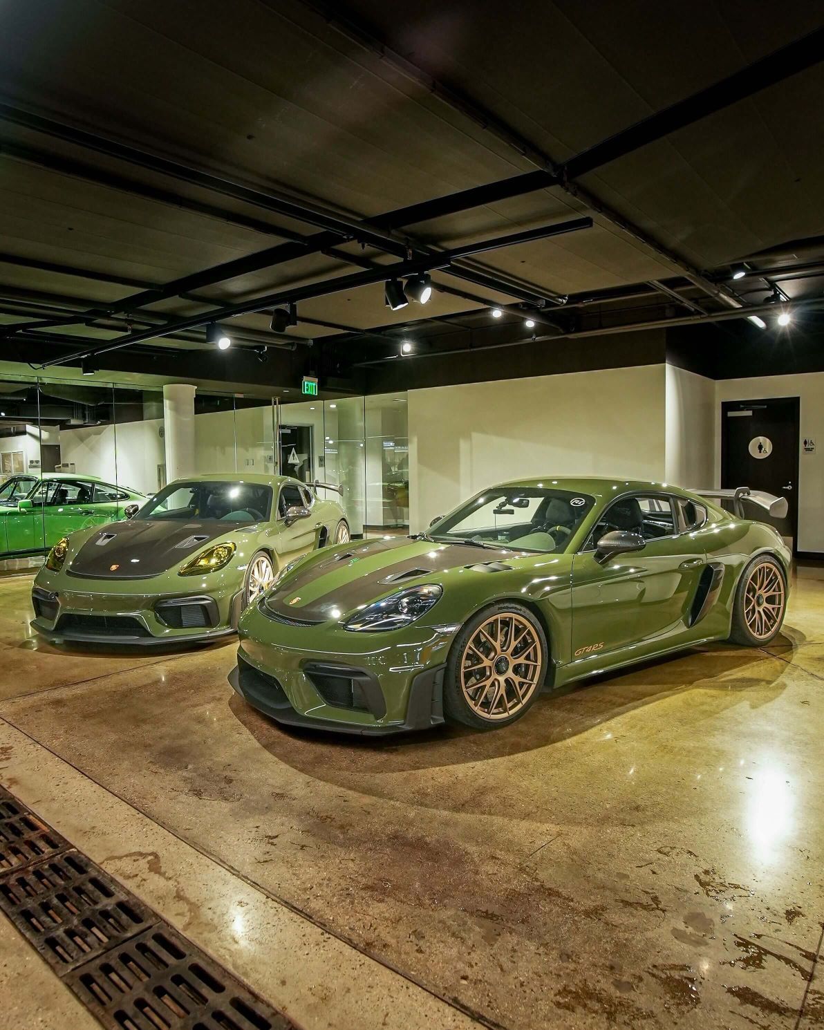 Two glossy green Porsche GT4 RS sports cars with gold wheels and racing stripes in a showroom.