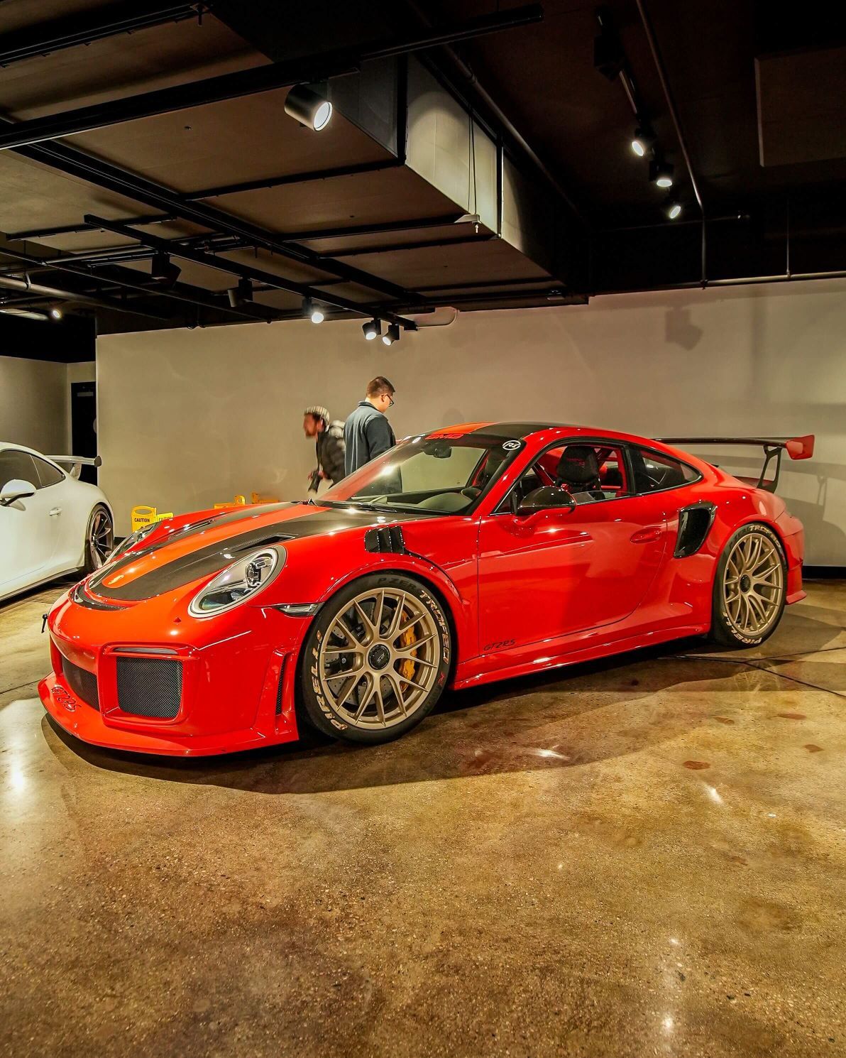A shiny red Porsche 911 GT2 RS with black and silver stripes, gold wheels, and a large rear spoiler in a showroom.