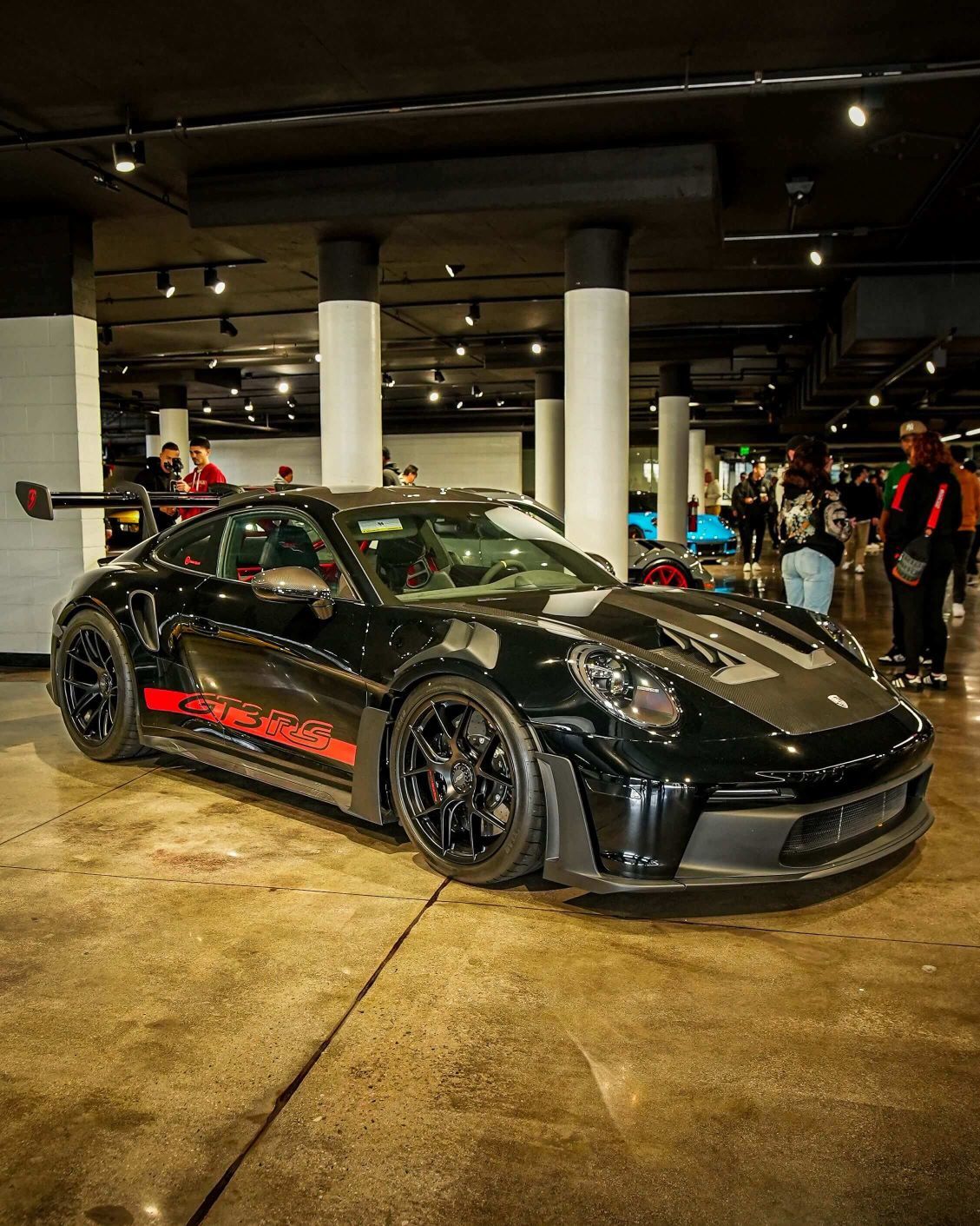 A black Porsche GT3 RS with red GT3 RS lettering on its side, parked on a concrete floor in
a low-lit room.