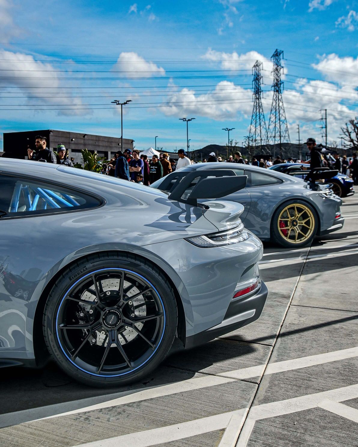 Two gray Porches with a rear view, parked on asphalt with people and power lines in the background.