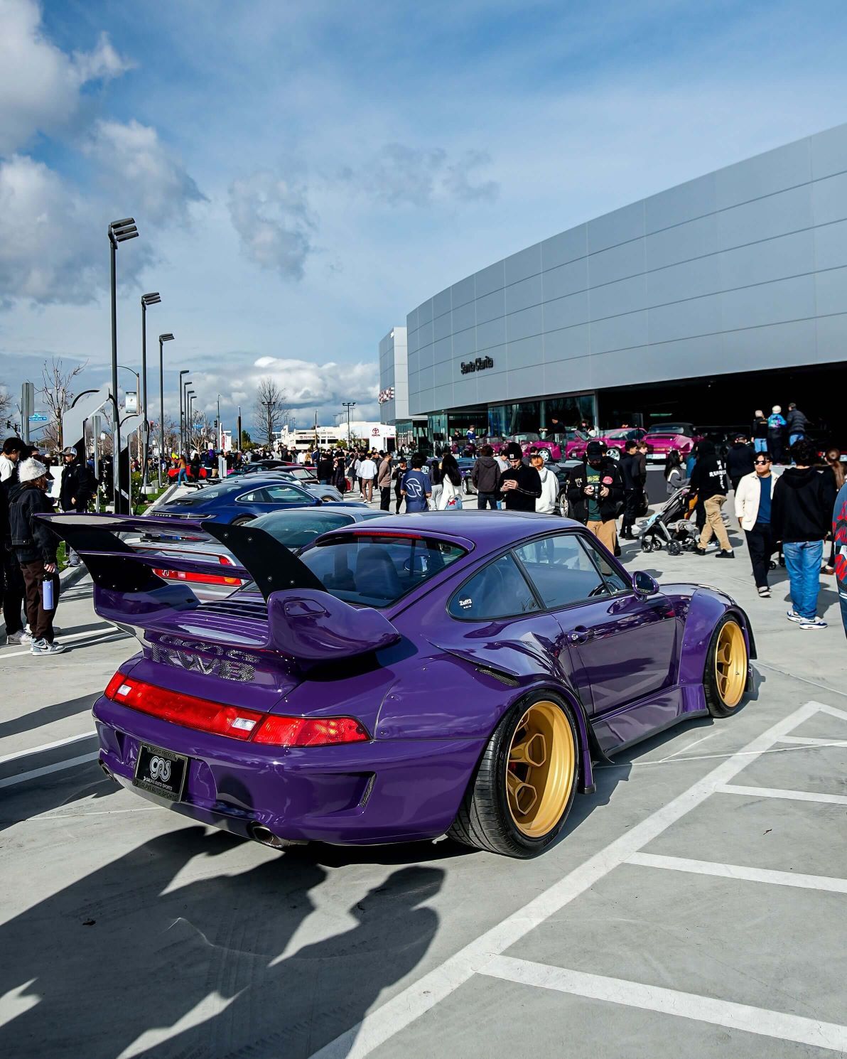 Purple Porsche 911 GT2 with gold wheels, wide fenders, and large rear spoiler at an outdoor car show.