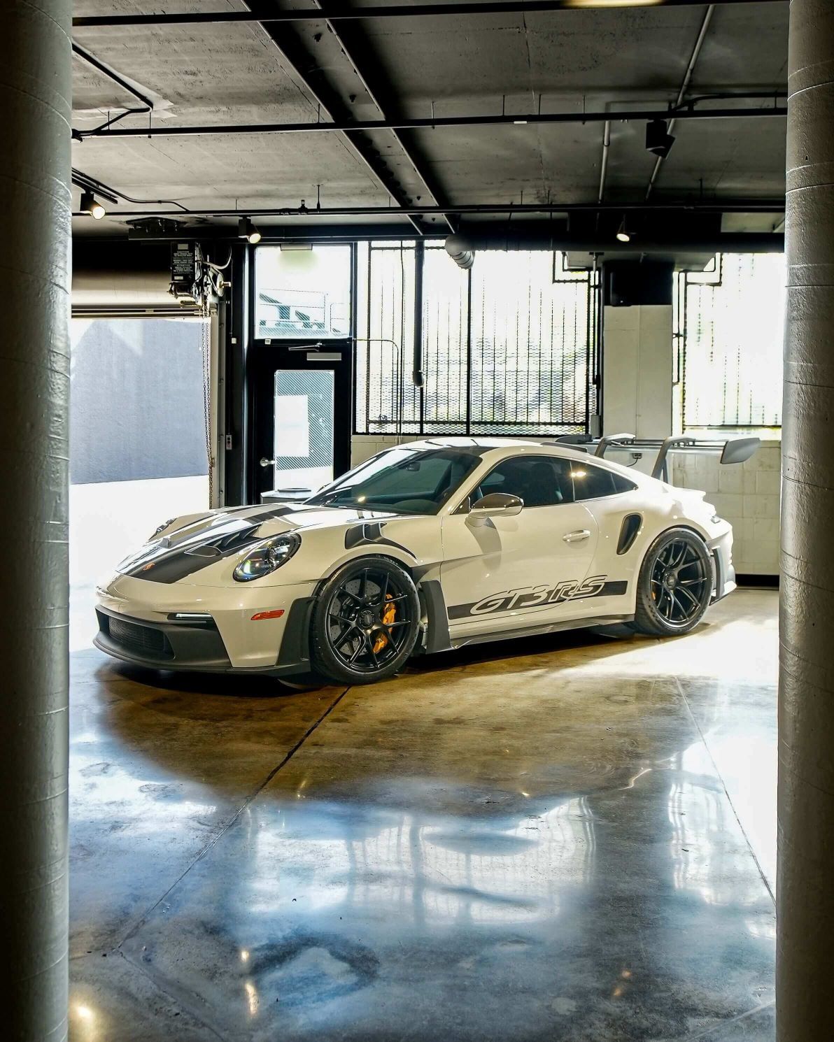 White Porsche 911 GT3 RS with black racing stripes parked on a reflective concrete floor in a modern garage.