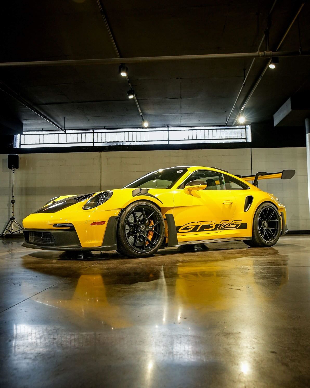 A bright yellow Porsche GT3 RS with black trim, spoiler, and wheels, parked on a reflective garage floor.