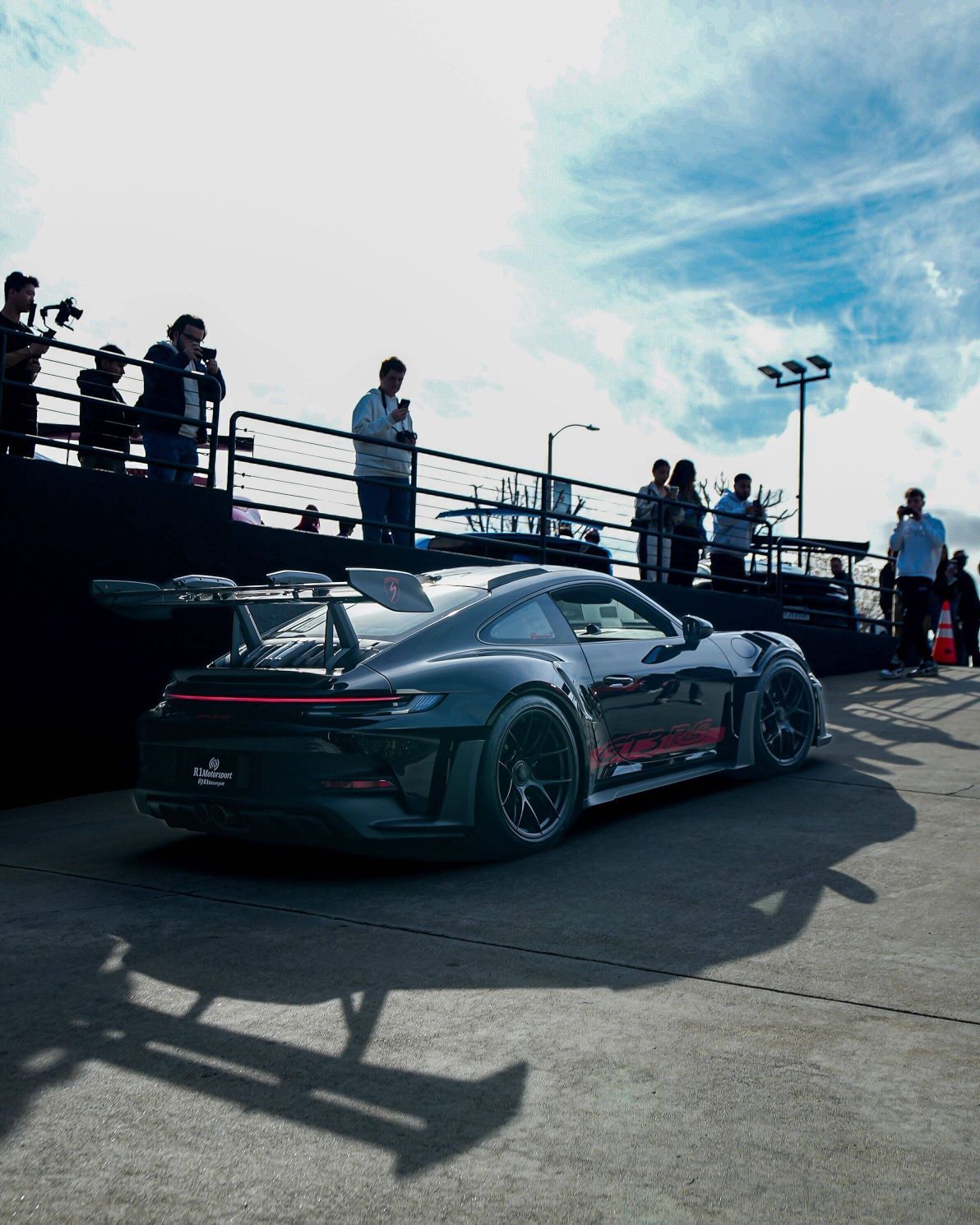 Rear view of a black Porsche 911 GT3 RS with a large spoiler and red accents, parked at an event.