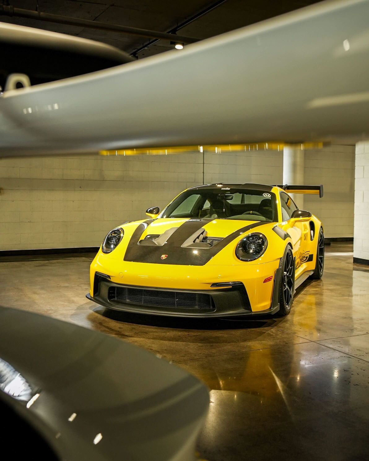 Bright yellow Porsche 911 GT3 with black racing stripes and spoiler, parked in an industrial garage.