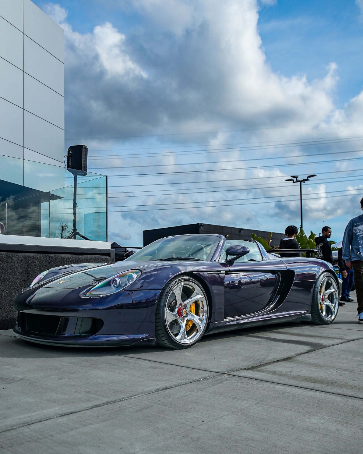 A sleek, dark purple Porsche Carrera GT with chrome wheels and yellow brake calipers, parked on concrete.