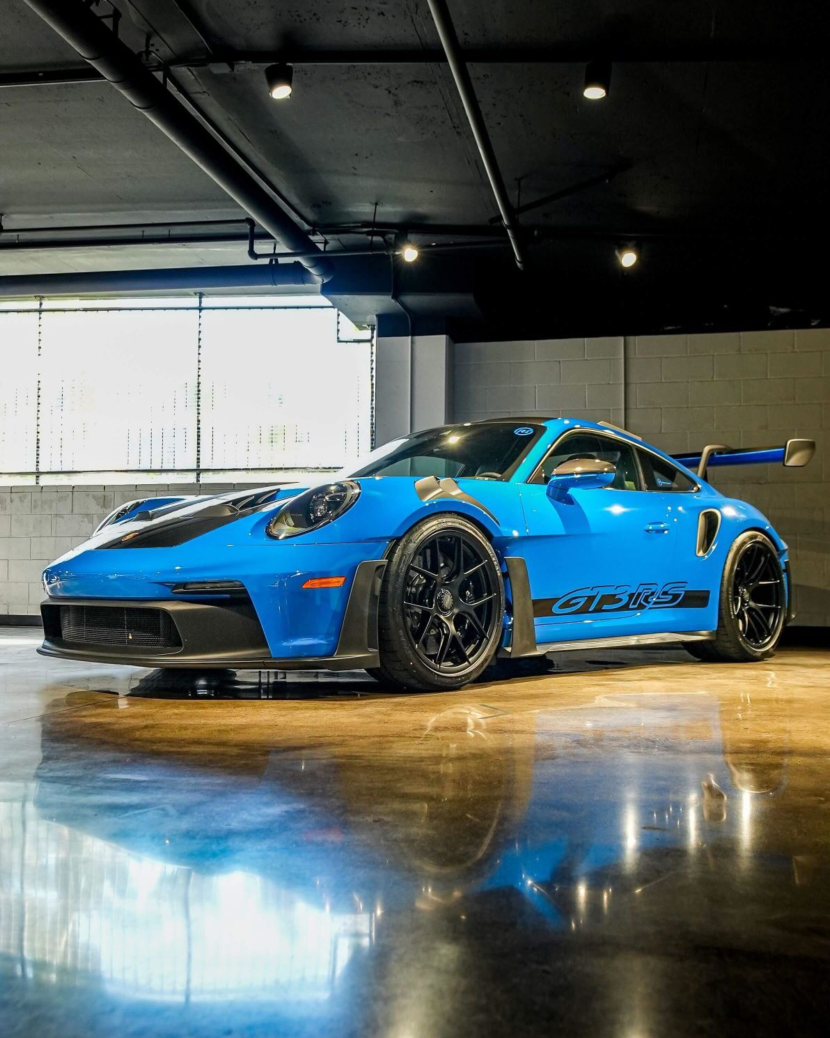 Bright blue Porsche 911 GT3 RS with black racing stripes parked on a glossy floor, reflecting the car.
