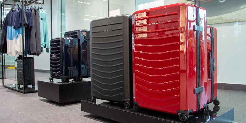 Several Porsche Design suitcases, including red, black, and blue, displayed in a brightly lit showroom.