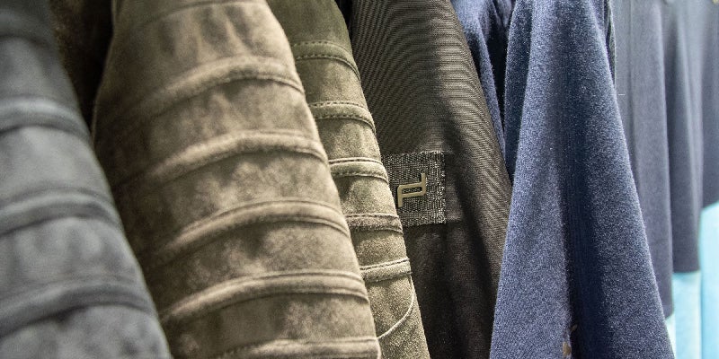 Close-up of clothes on a rack, showing shades of gray, olive green, black, and blue fabrics.