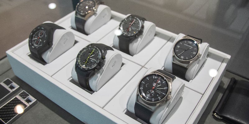 Six men's wristwatches with black bands and dials, displayed on white risers in a lighted case.