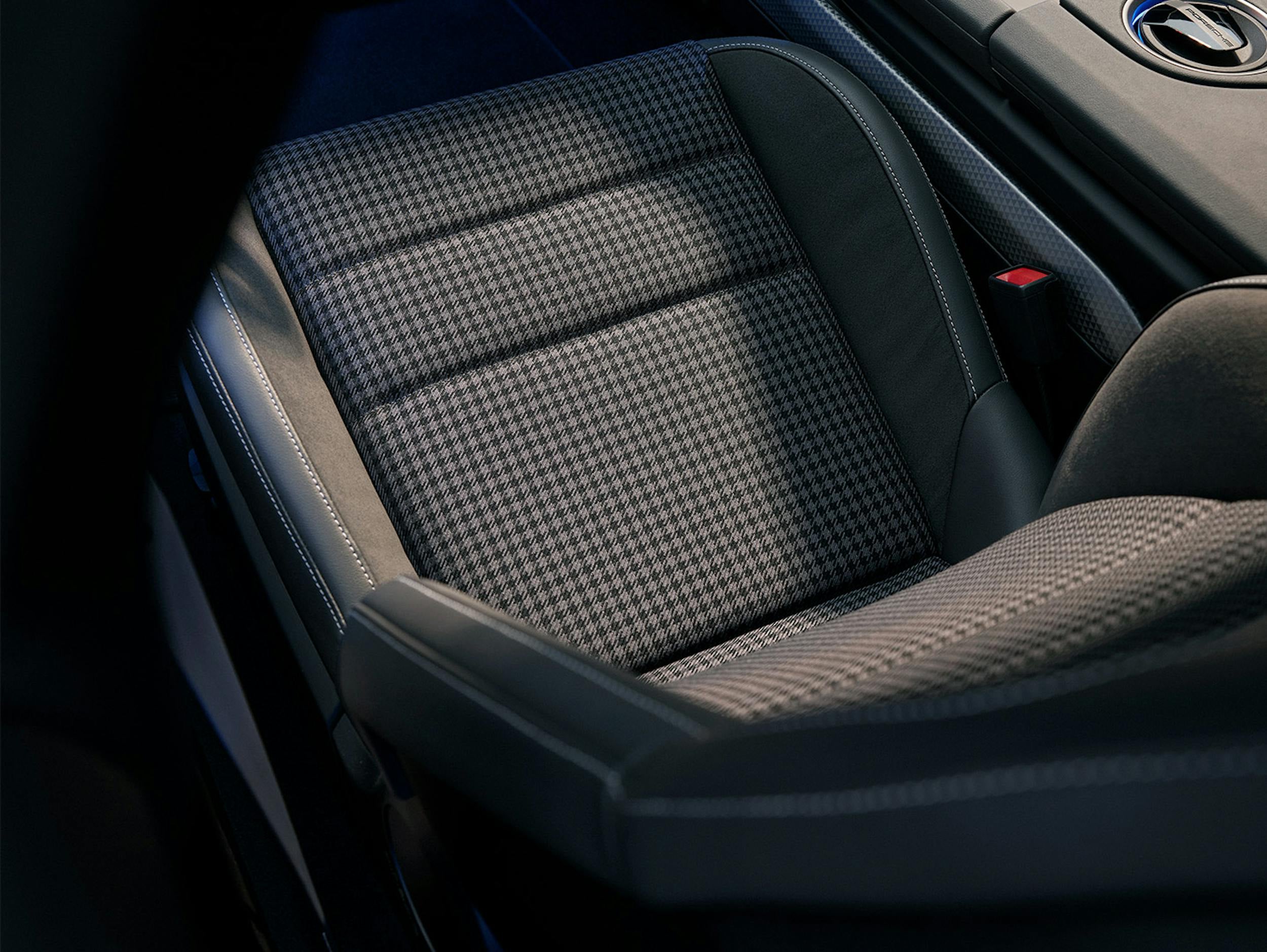 Close-up of a Porsche car seat featuring a houndstooth-patterned fabric in the center, surrounded by black leather with visible white stitching.
