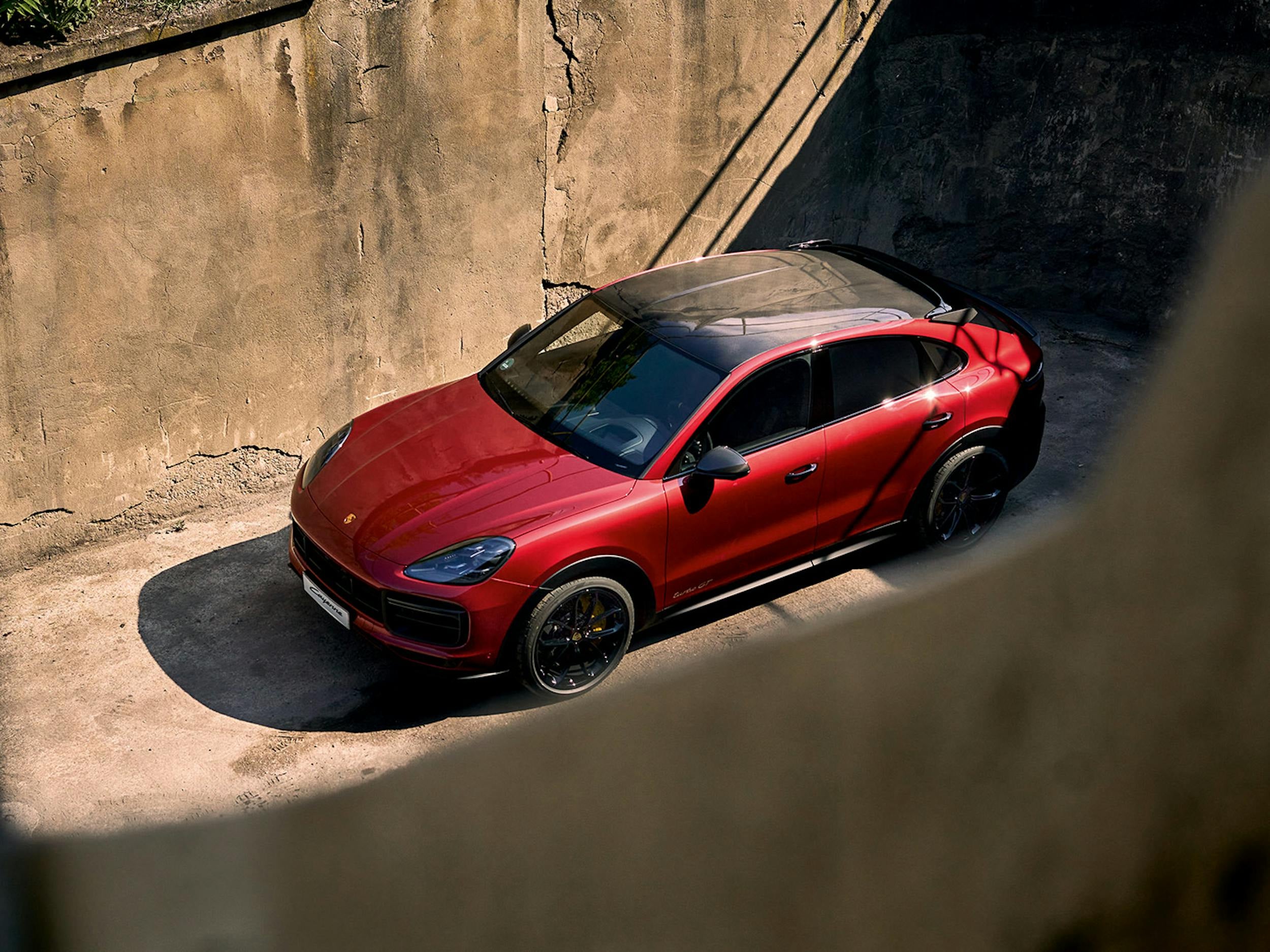 A red Porsche Cayenne Coupe parked between tall concrete walls.